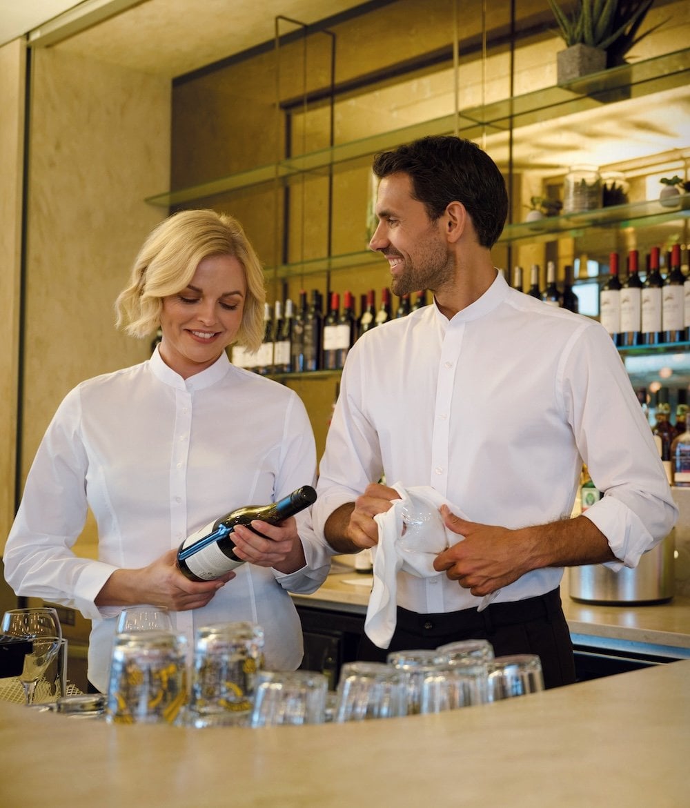 A male and female waiter at a wine bar wearing white shirts
